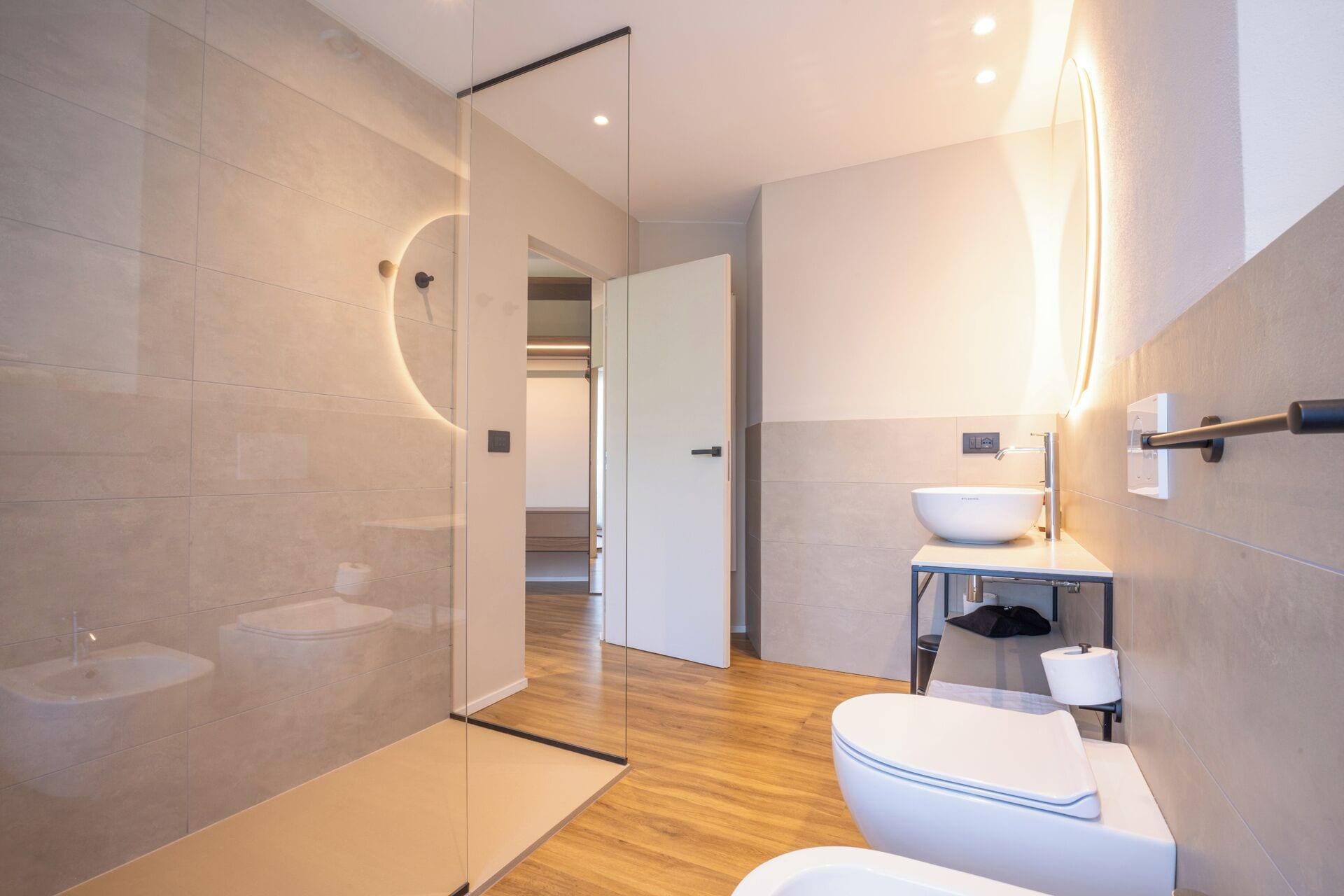 A modern bathroom with a glass shower enclosure, a toilet, a sink, and a mirror with integrated lighting.