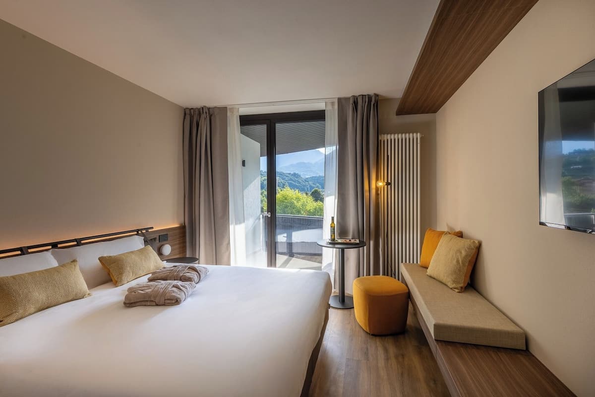 Una camera d'albergo con un letto, un'area salotto vista e una finestra con tende.