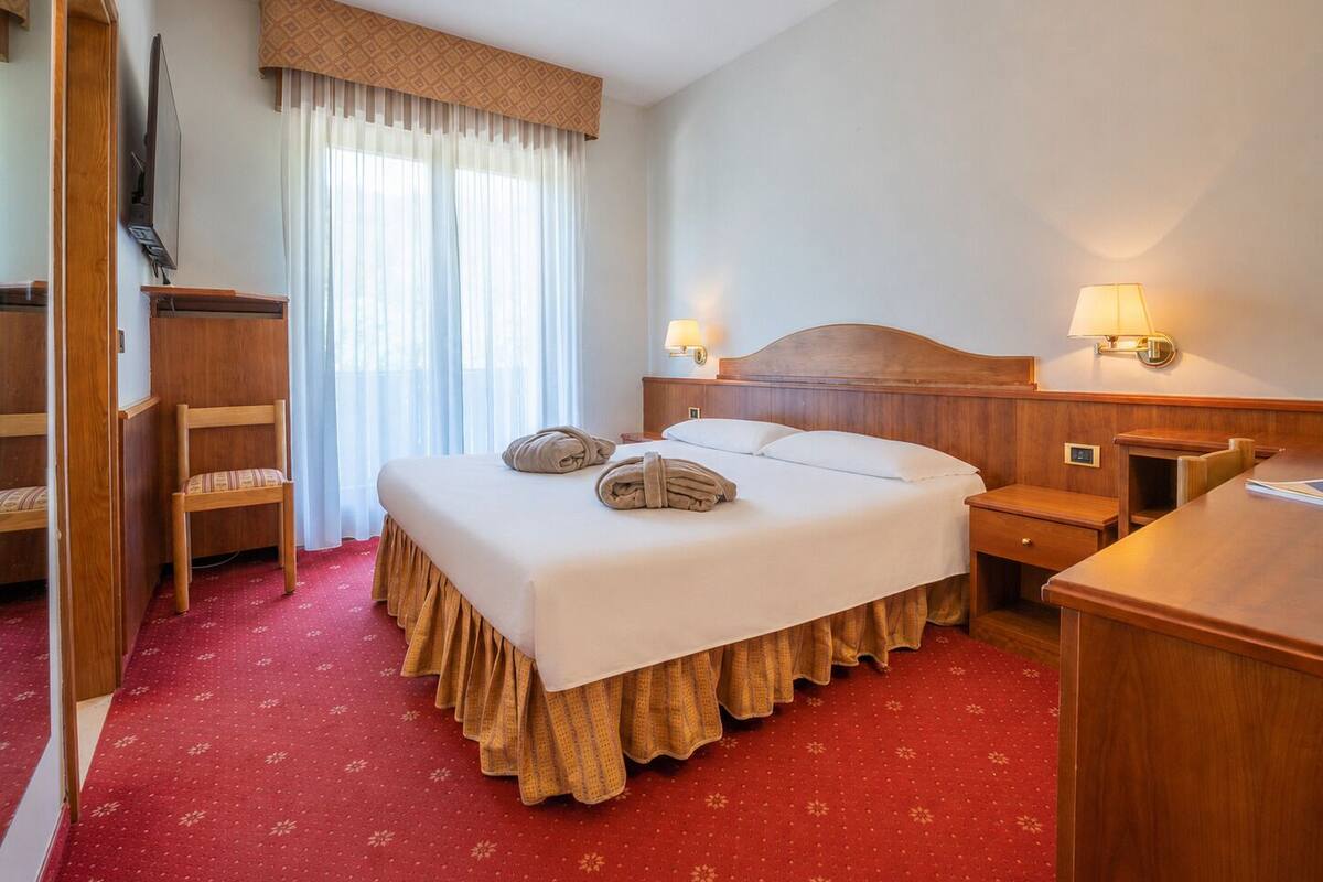 Una camera d'albergo con un letto, una scrivania, una sedia, un armadio e una finestra con tende.