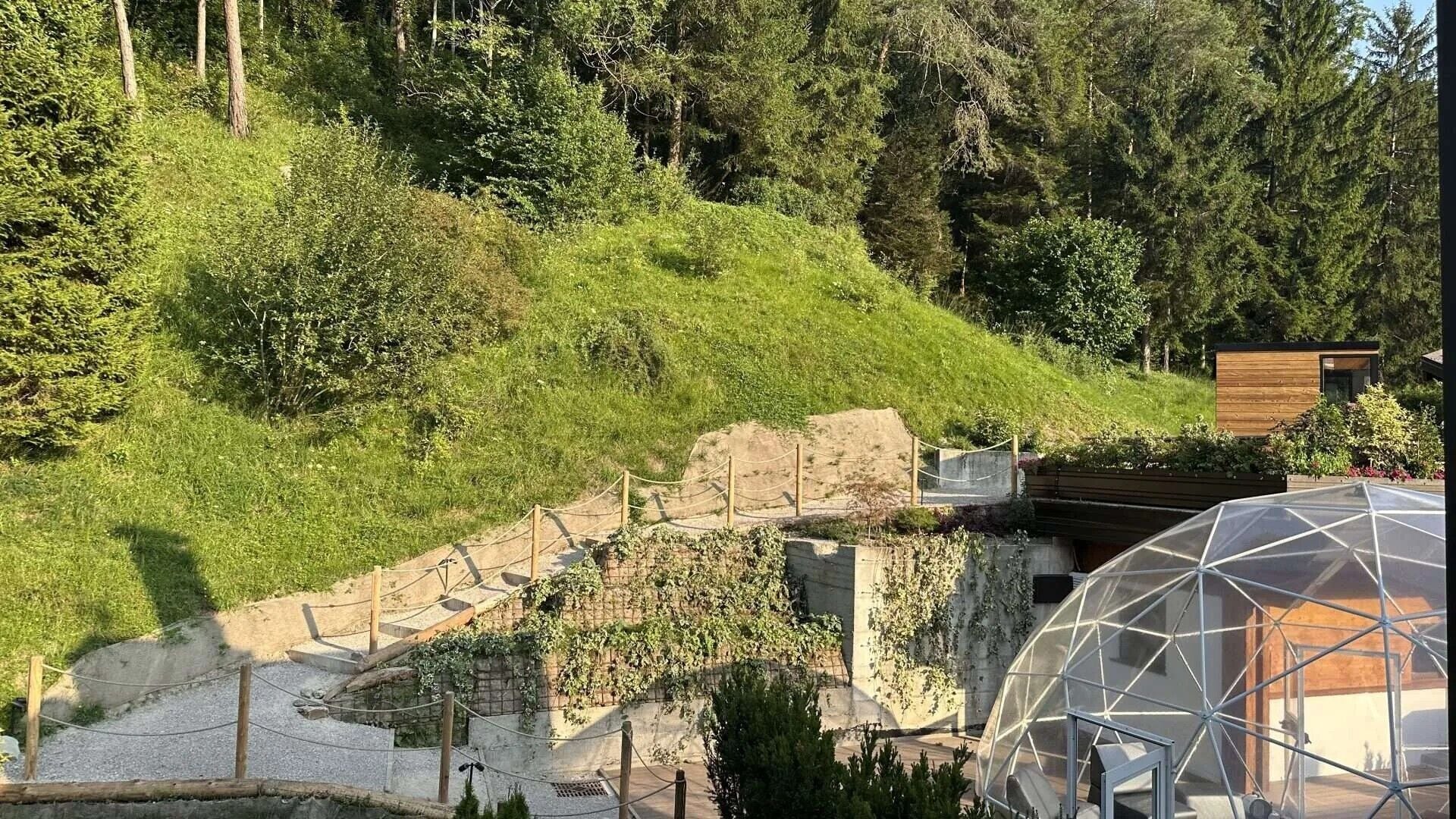 Un jardín en terrazas con una estructura de madera y una cúpula geodésica.