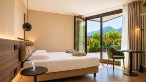 Una habitación de hotel moderna con una cama, una mesita, una silla y vistas a montañas a través de amplios ventanales.