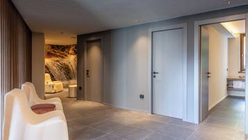 A modern hotel lobby with a seating area, a stone wall with a waterfall image, and a view into a bathroom.