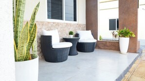 Een terras met rieten stoelen en een kleine tafel, omringd door potplanten.