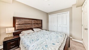 Quarto com cama, mesa de cabeceira, abajur e guarda-roupa.