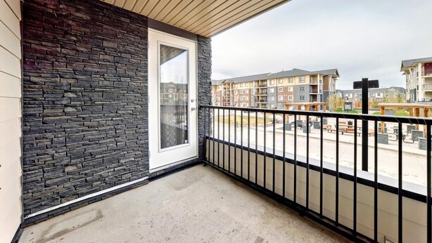Varanda com parede de pedra, porta de vidro e vista para área residencial com edifícios de apartamentos.