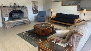 A living room with a stone fireplace, a blue armchair, a sofa, a coffee table, and a lamp. - Chisos Mining Co Motel (Terlingua)