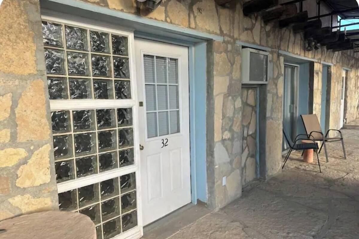 A stone building with a white door marked '32', a window with frosted glass, and a chair outside.