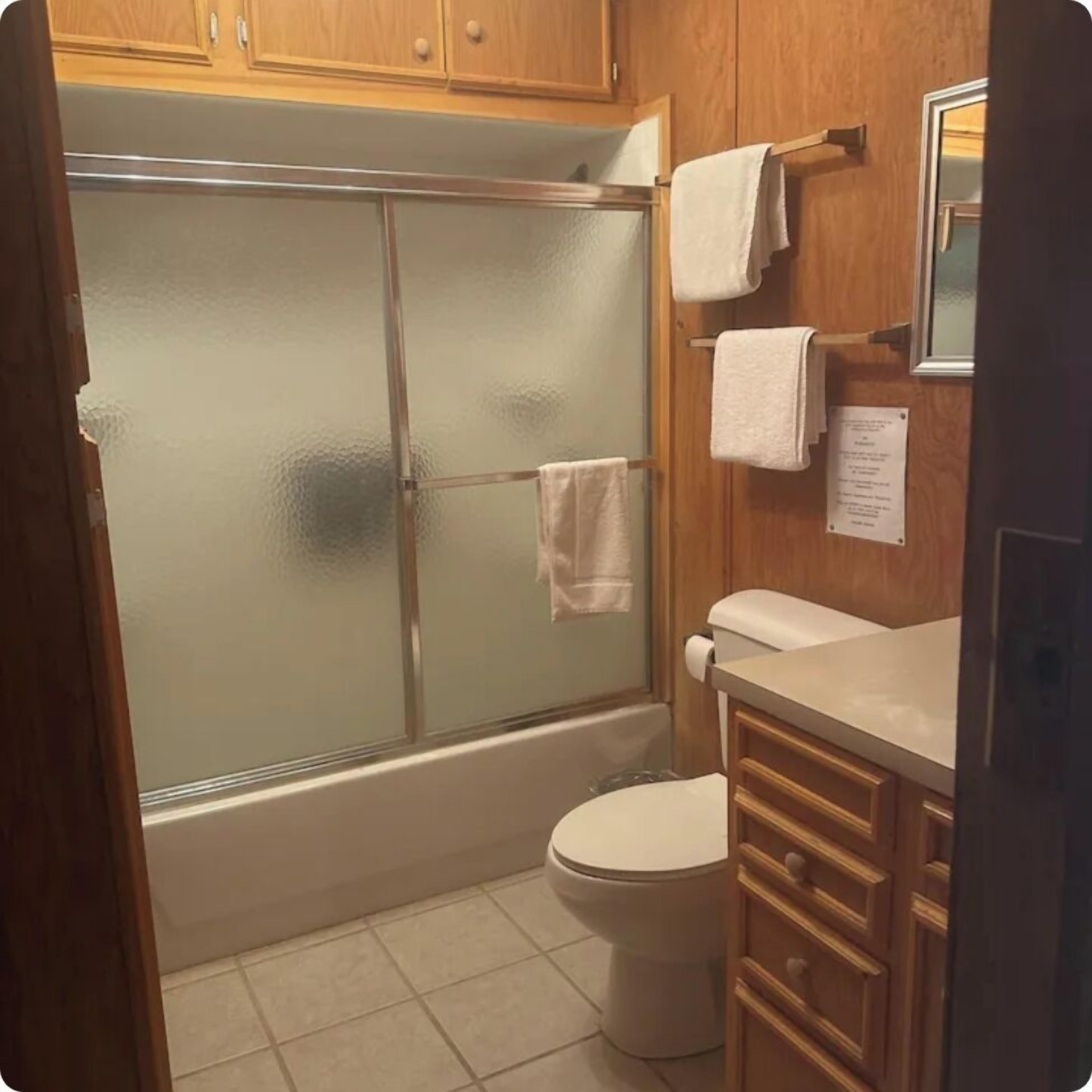 A bathroom with a glass-enclosed shower, a toilet, and wooden cabinets.