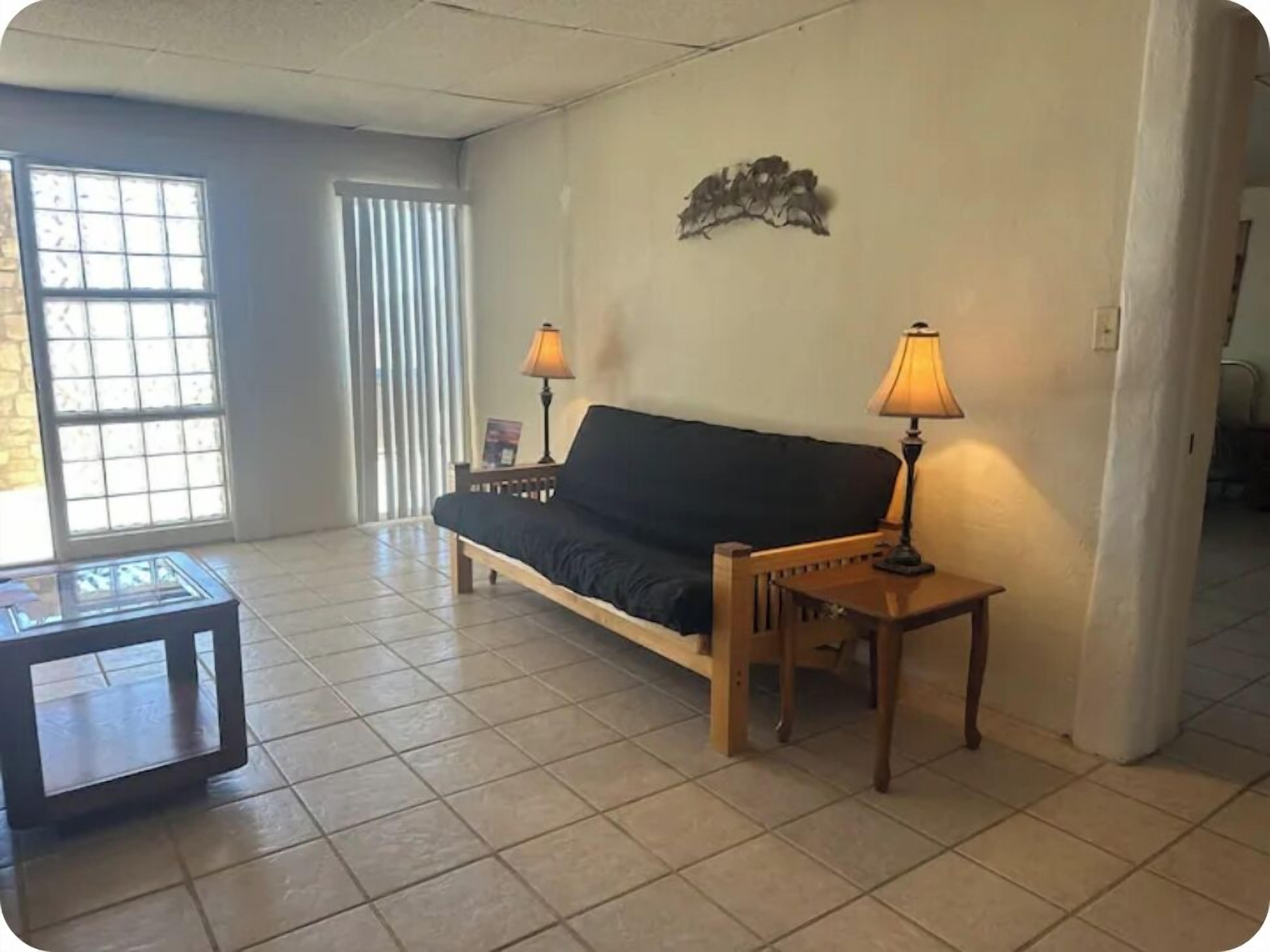 A living room with a sofa, two lamps, a small table, and a window with blinds.