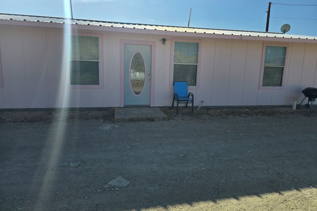A single-story building with a pink exterior, a front door, and a blue chair outside.