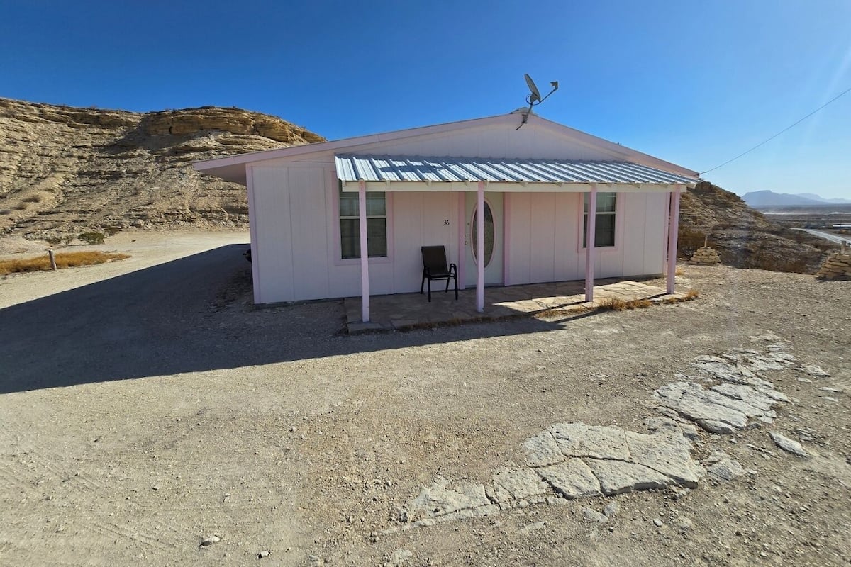 A small, single-story building with a metal roof, a porch with a chair, and a satellite dish.