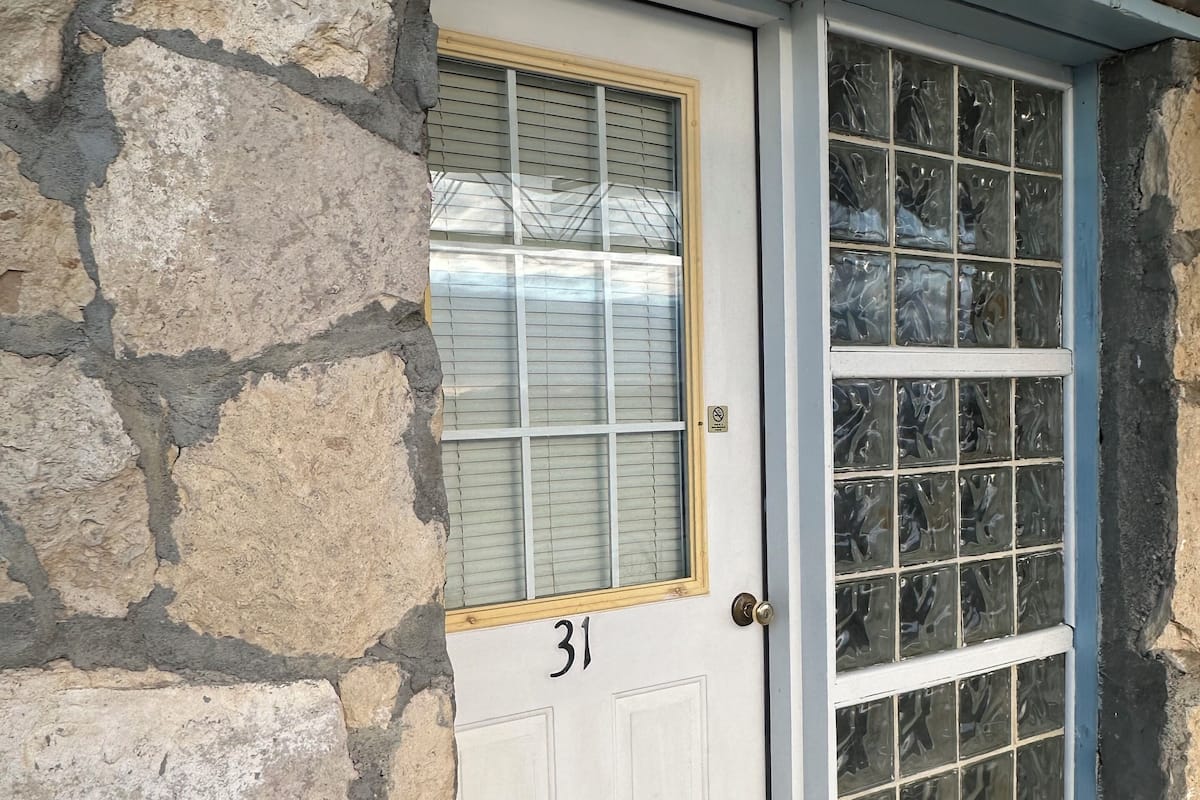 A white door with the number 31, a window with blinds, and a stone wall.
