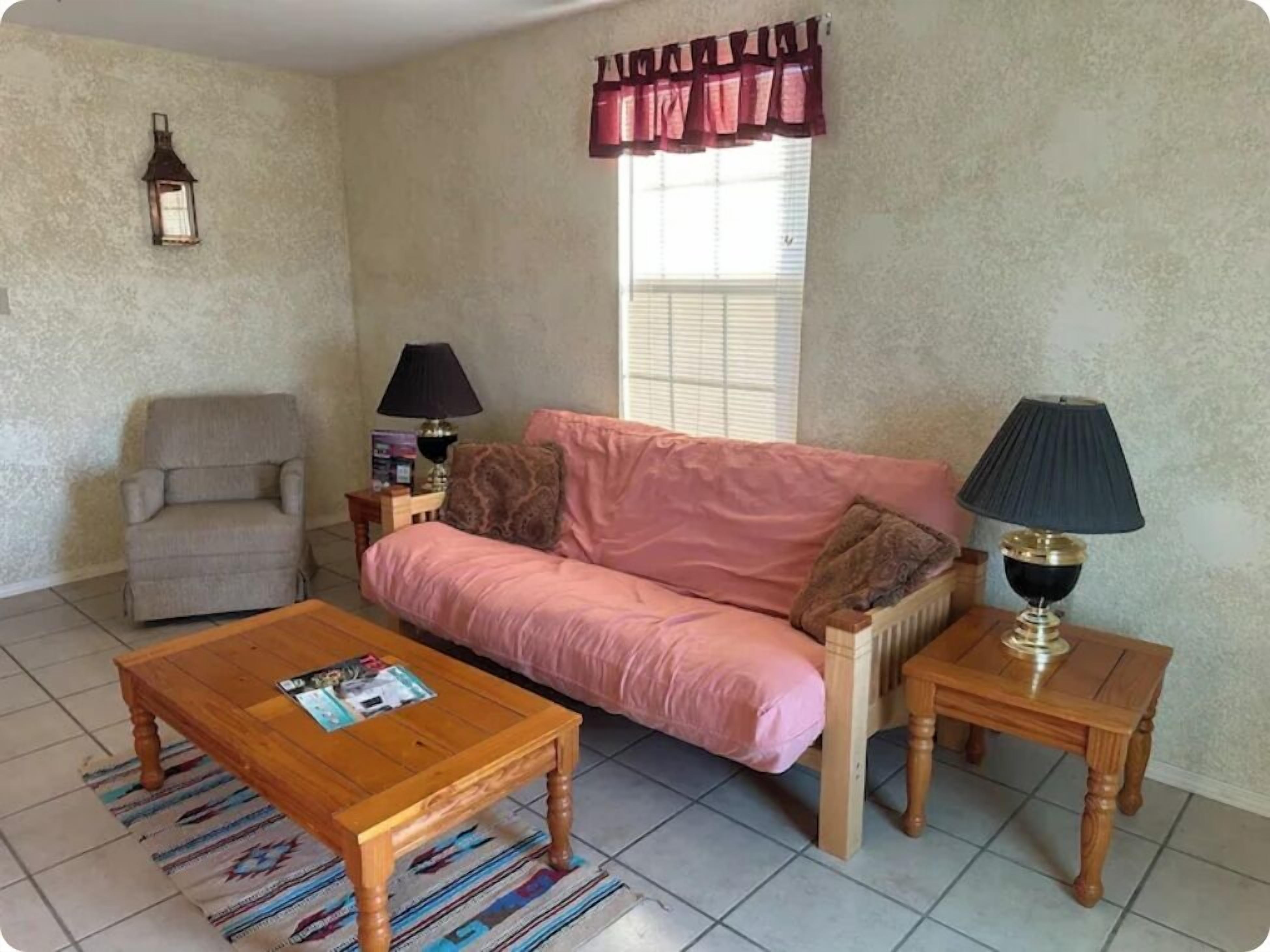 A living room with a pink sofa, a wooden coffee table, a side table with a lamp, a chair, and a wall-mounted lantern.