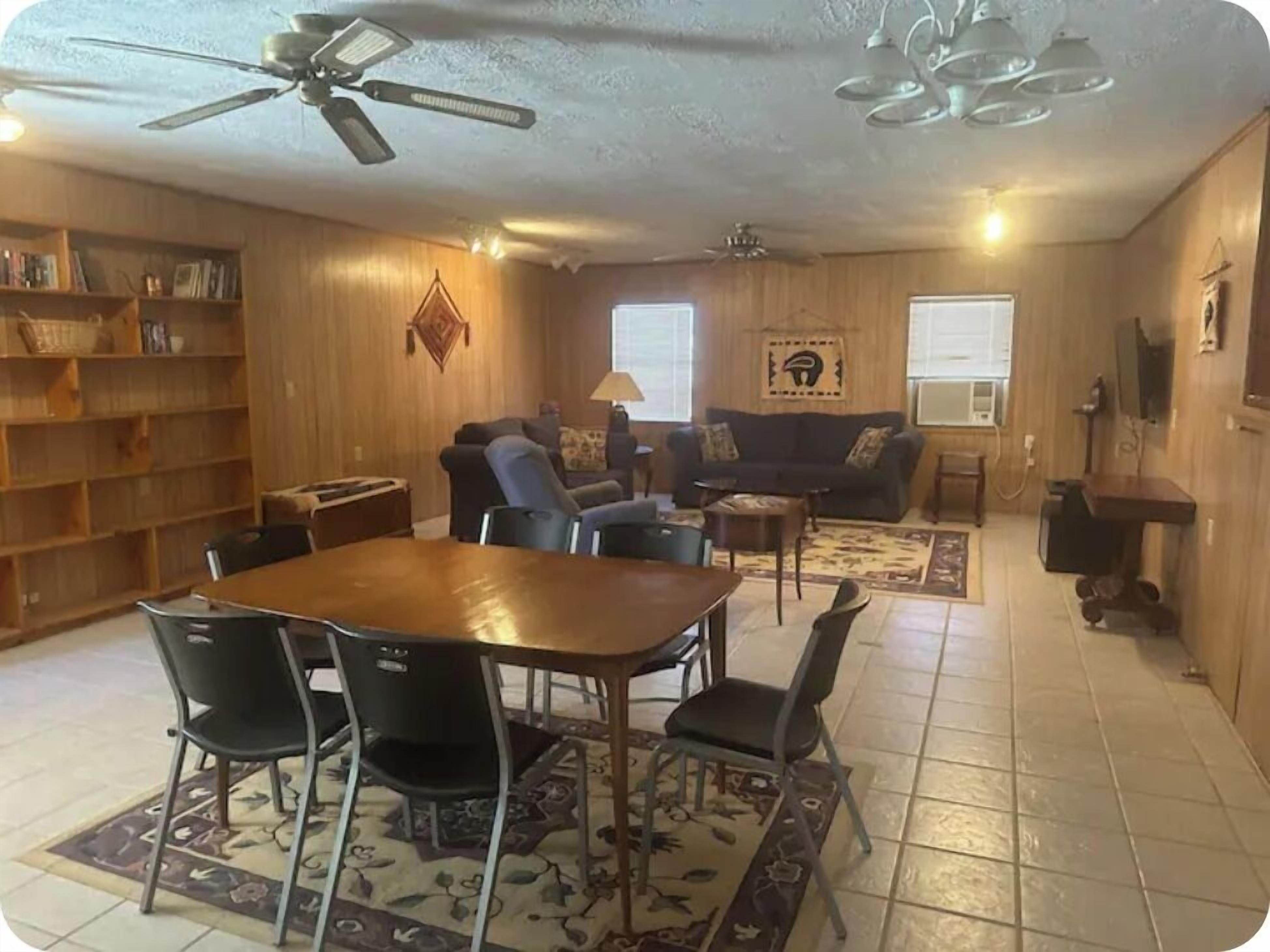 A spacious living room with a wooden floor, a dining table with chairs, a sofa, and a ceiling fan.