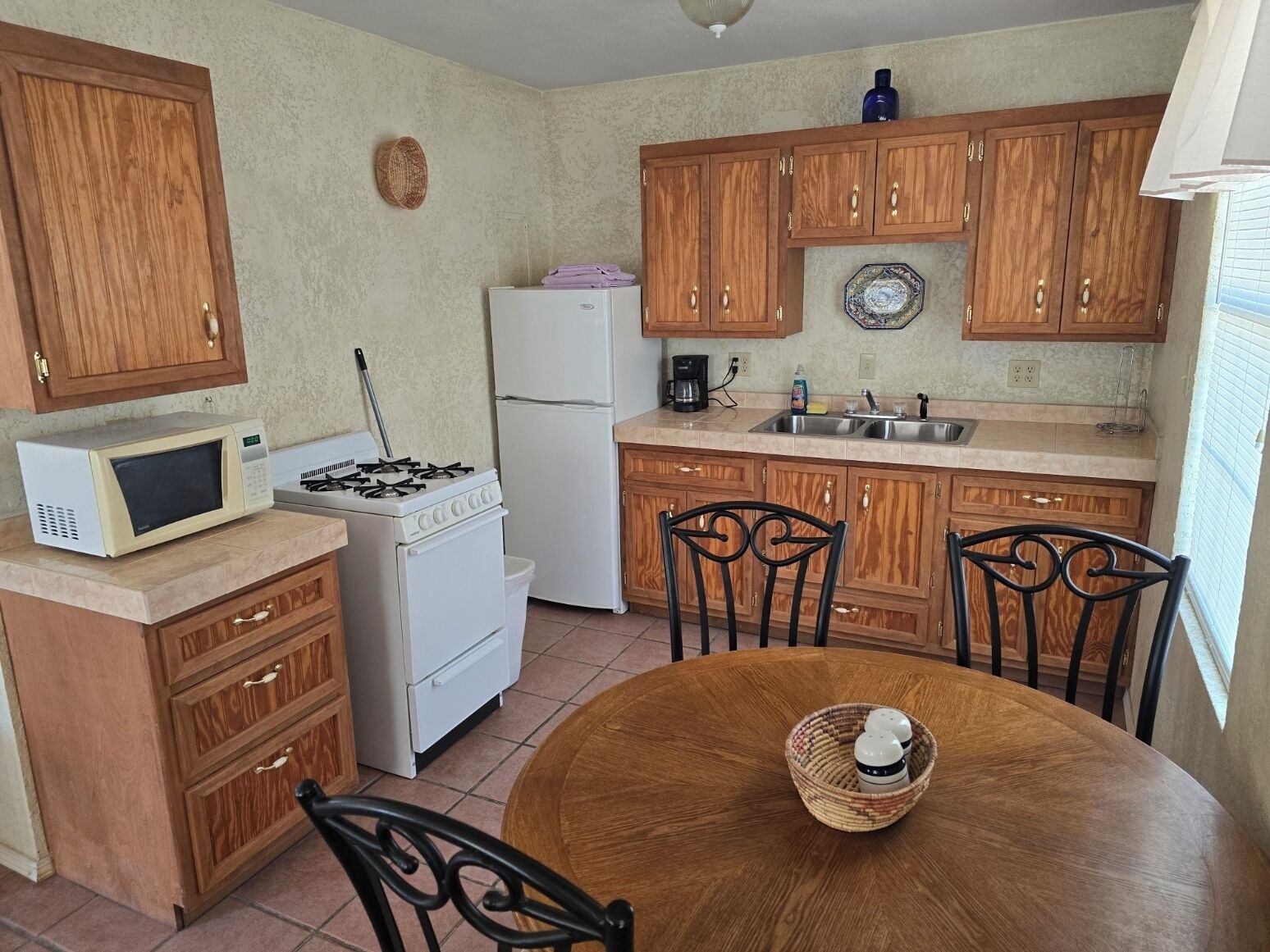 A compact kitchen with wooden cabinets, a white stove, a microwave, a refrigerator, and a dining table with chairs.