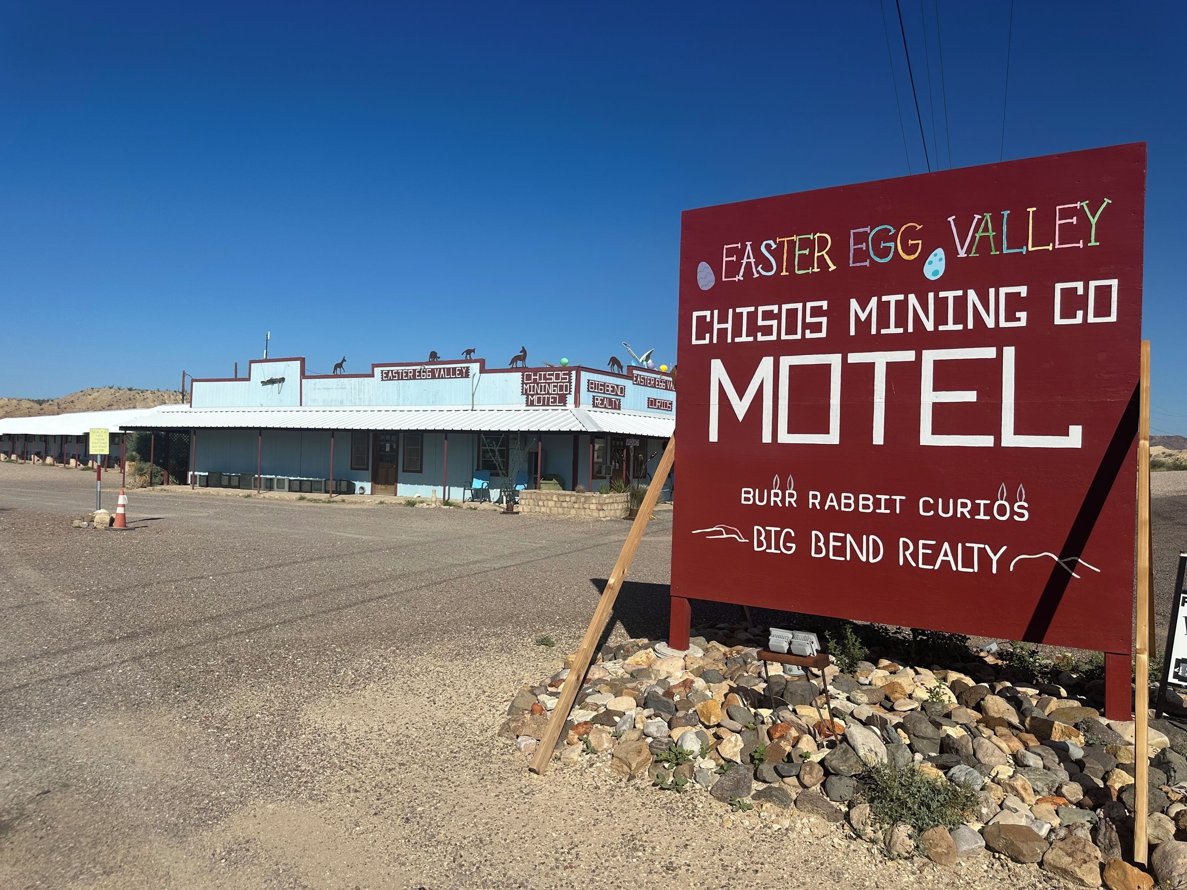 A motel sign with the name 'Easter Egg Valley Chisos Mining Co Motel' and mentions 'Burr Rabbit Curios' and 'Big Bend Realty.'