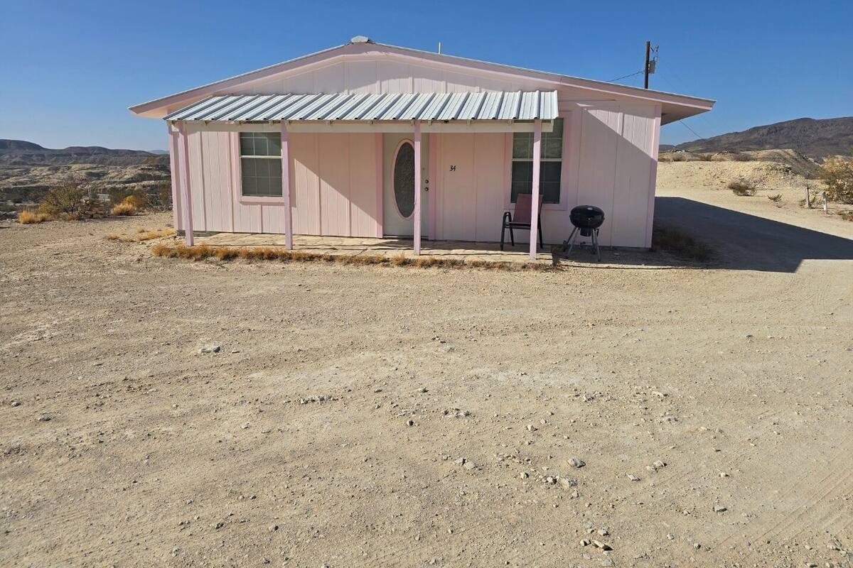 A pink single-story building with a metal roof, a small porch, and a number '34' on the door.