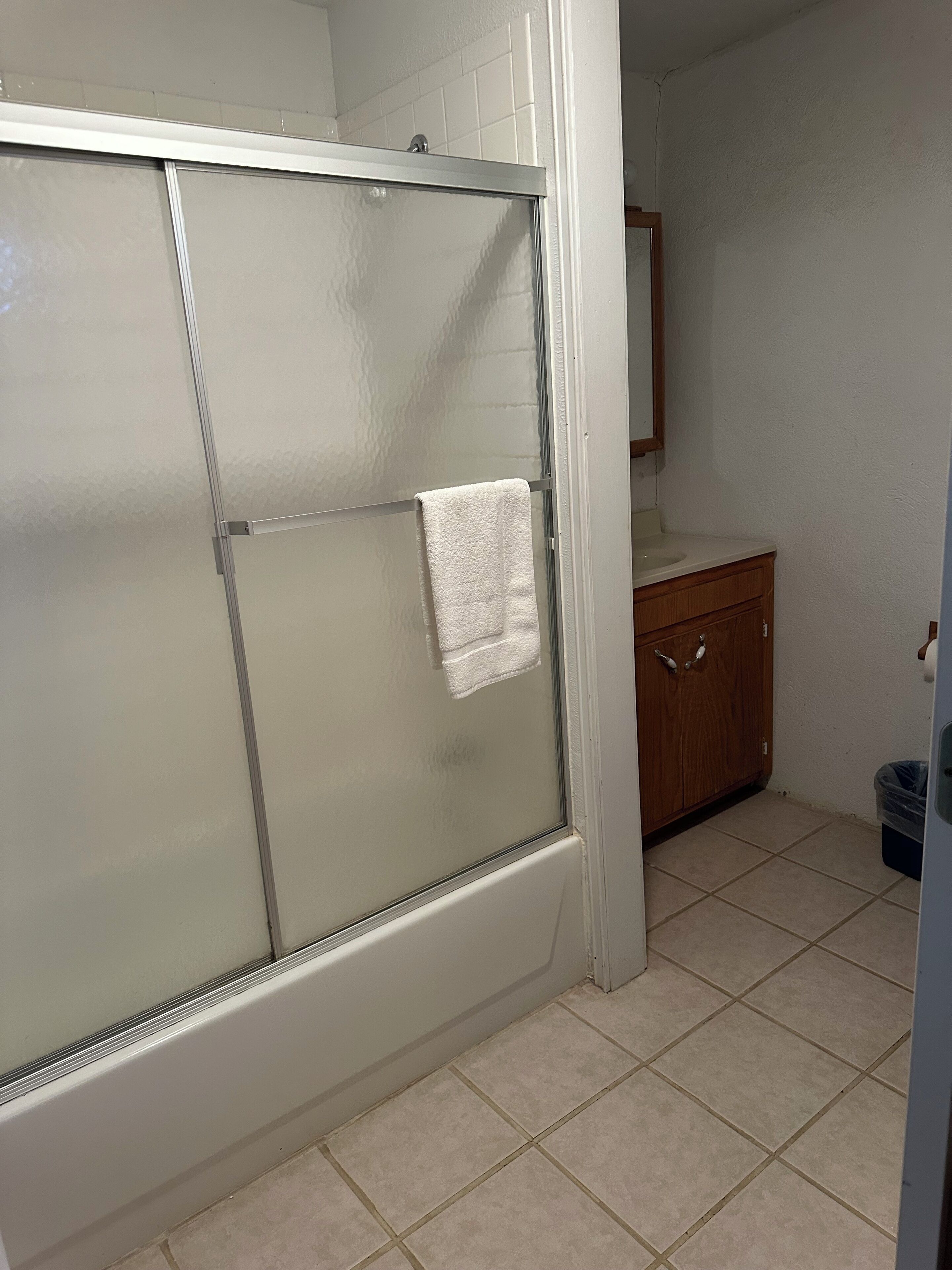 A bathroom with a glass shower enclosure, a wooden vanity, and a tiled floor.
