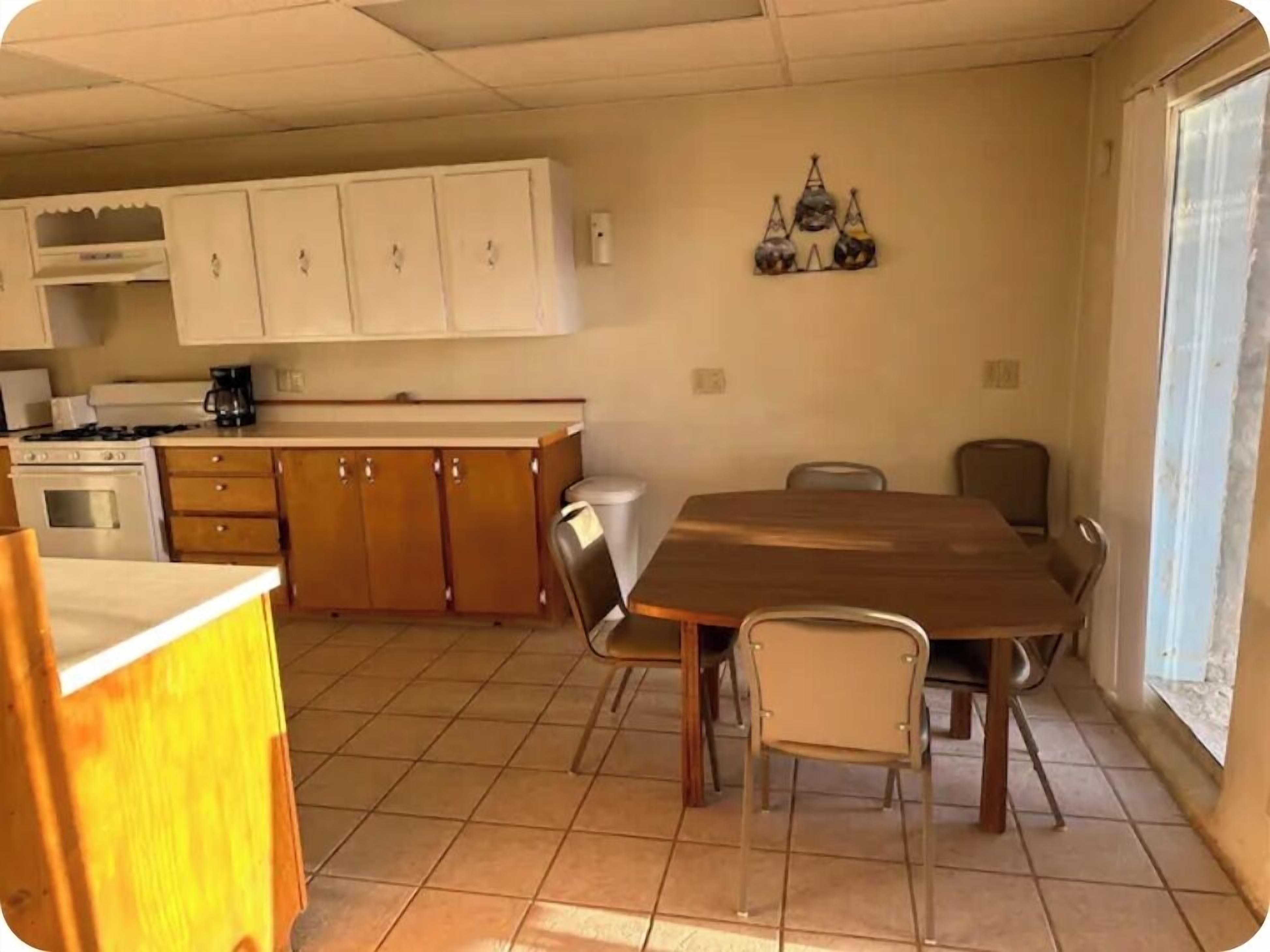 A dining area with a wooden table and chairs, a kitchen with white cabinets, and a decorative wall hanging.
