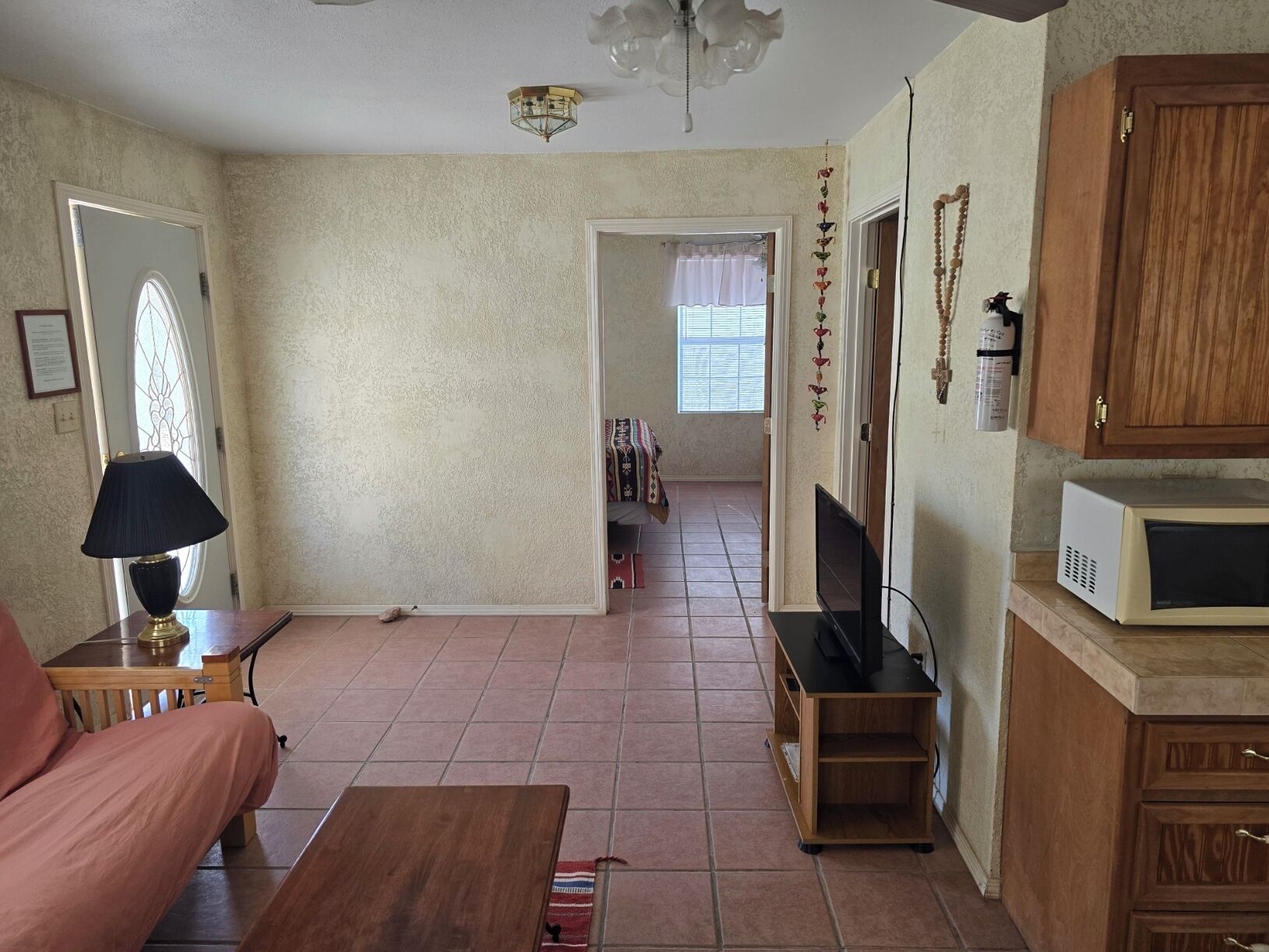 A living room with a sofa, a coffee table, a TV, wooden cabinets, a microwave, and a door leading to another room.
