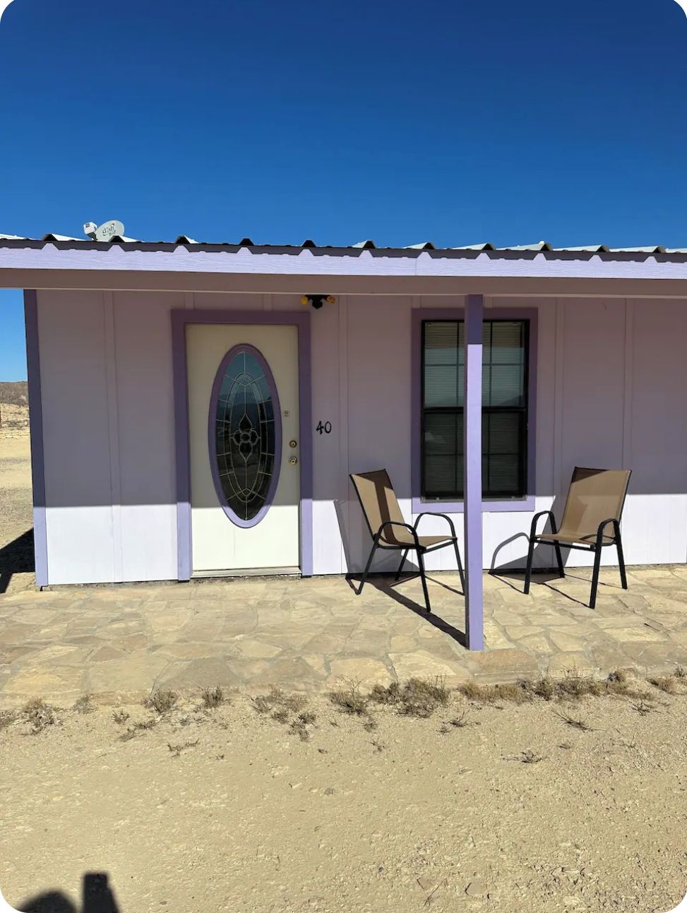 A small, single-story building with a white exterior and a purple door. There are two chairs outside the building, and the number 40 is visible on the wall.