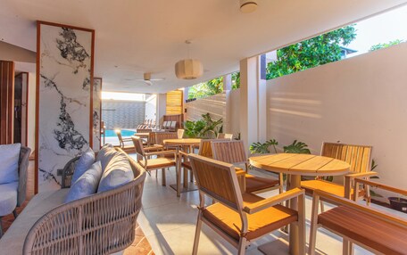 A modern outdoor dining area with wicker furniture and wooden tables, overlooking a pool and lush greenery.