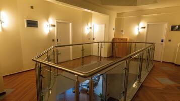 A spacious hallway with a glass railing, wooden flooring, and multiple doors.