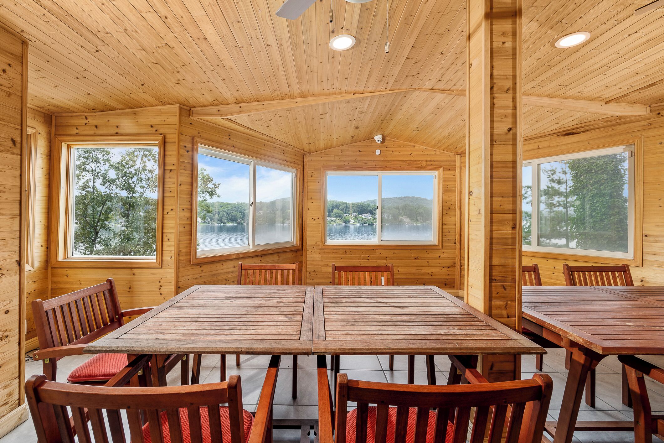 A wooden cabin with a large dining table and chairs, large windows with views of trees and hills.