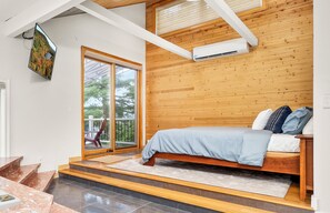 A modern bedroom with a bed, wooden panel walls, a large window, and a sliding glass door leading to a balcony. - North Cliff House - Private Dock & Sauna (Danbury)