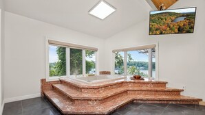Een ruime badkamer met een groot ligbad, een raam met uitzicht op groen en een flatscreen tv aan de muur bevestigd.