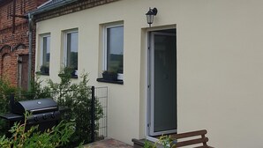 Ein Haus mit Ziegeldach, Satellitenschüssel, Grill und einem Holztisch mit einem Glas.