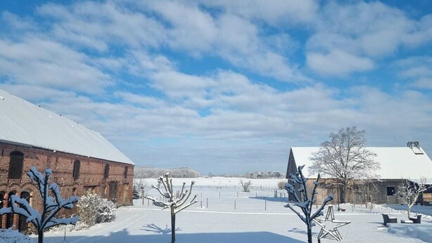 Eine verschneite ländliche Landschaft mit einem Backstein- und einem Holzstall, und einem klaren Himmel.