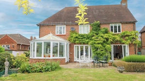 A brick house with a conservatory, a garden, and a patio with outdoor furniture.