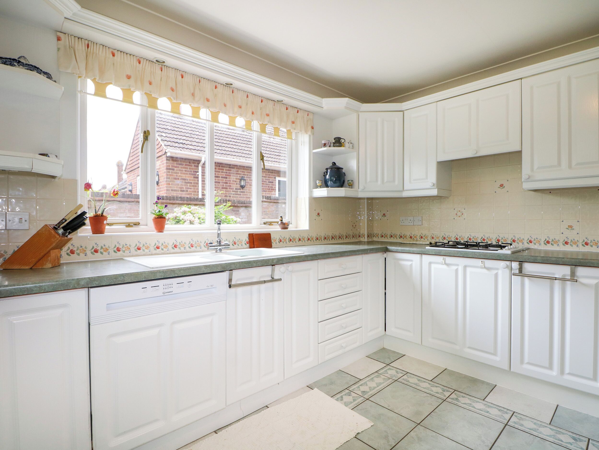 A kitchen with white cabinets, a window with a floral curtain, a sink, and a stove.