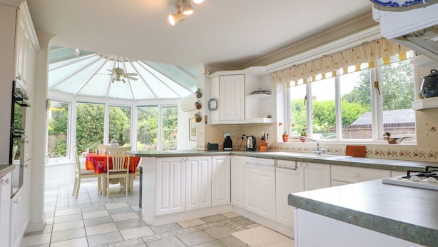 A bright kitchen with white cabinets, a dining area with a table and chairs, and a large window offering a view of greenery.