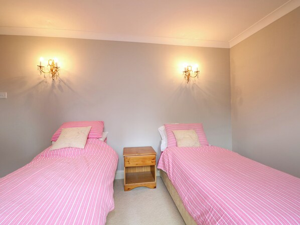 A bedroom with two single beds, each with pink bedding and white pillows. There is a wooden nightstand between the beds. - Little Birches (Tenterden)