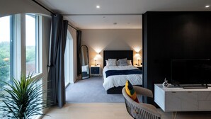 Habitación de hotel moderna con una cama grande, televisión, escritorio y vistas al exterior.