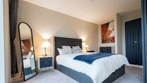 Una habitación de hotel moderna con una cama grande, lámparas de noche, una mesita de noche, un espejo y un cuadro en la pared.