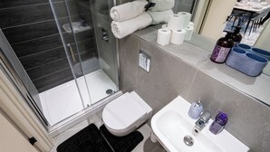 Un baño moderno con cabina de ducha de vidrio, inodoro, lavamanos con espejo y artículos de aseo en la encimera.