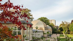 A botanical garden with a large glass greenhouse and a classical building with a dome.