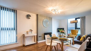 A modern dining area with a glass table, white chairs, and a decorative mirror on the wall.