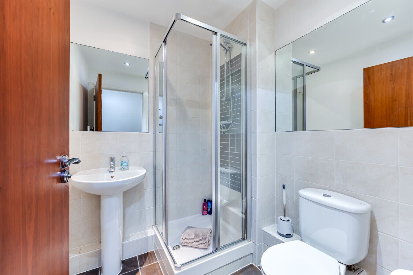 A modern bathroom with a glass shower enclosure, a pedestal sink, a toilet, and a mirror.