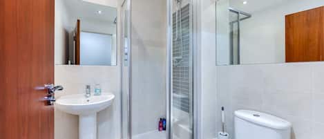 A modern bathroom with a glass shower enclosure, a pedestal sink, a toilet, and a mirror.