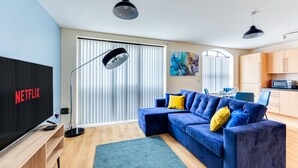 Un salon moderne avec un canapé d’angle, un téléviseur à écran plat et un grand lampadaire.