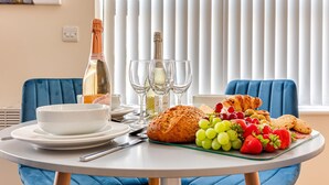 Une table mise pour le petit-déjeuner, avec une place pour deux personnes, comprenant des croissants, des raisins, des fraises et du pain.