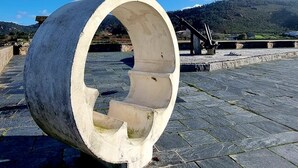A large concrete structure with a circular opening, set on a stone-paved area with a clear blue sky and distant hills in the background. - PERIPLO HOME (Camelle)