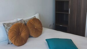 En säng med vita sängkläder, två stora bruna kuddar och en turkos kudd. En mörk trägarderob står till höger.