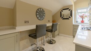A kitchen with a large wall clock, two bar stools, a window with flowers, and a sink. - Moat House Penthouse Suite - 2 Bed  2 Bath (Rawtenstall)