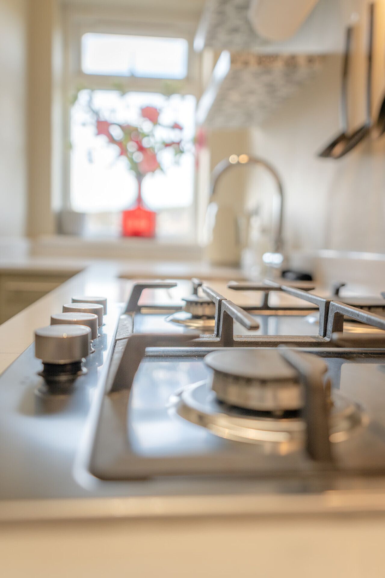 A kitchen with a gas stove, a sink, and a window with a view of a garden.