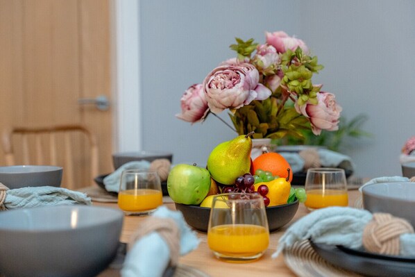 A dining table with a fruit bowl, glasses of orange juice, and a vase of flowers.